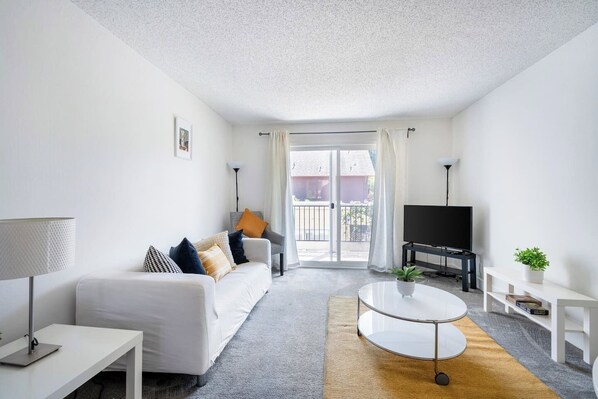 Un salón moderno con un sofá blanco, una mesa de centro, un televisor y un balcón con vistas.