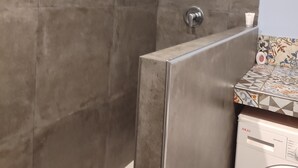 Baño con ducha a ras de suelo, lavadora y paredes de azulejos.