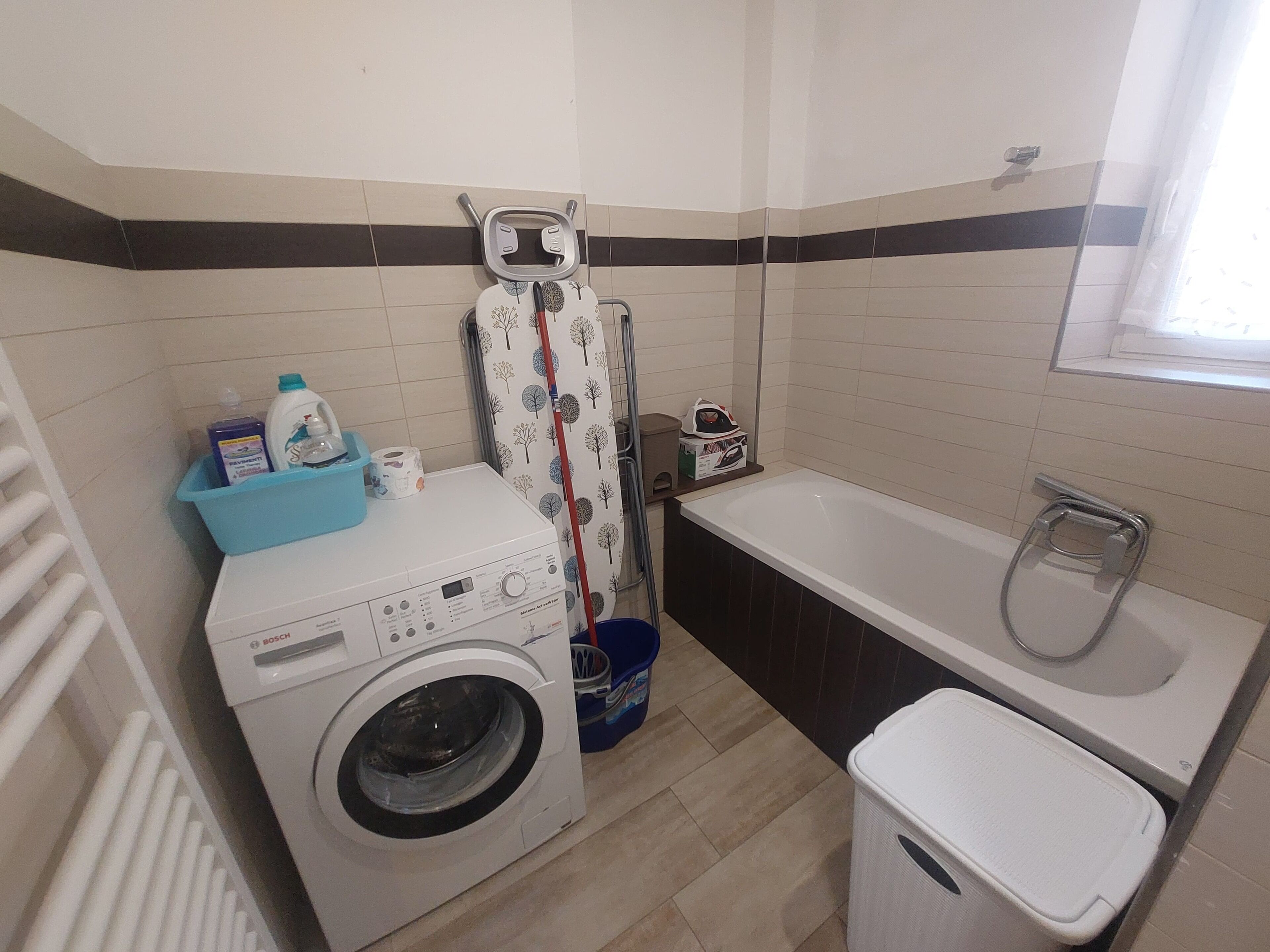 A compact bathroom with a Bosch washing machine, a bathtub, and a shower.