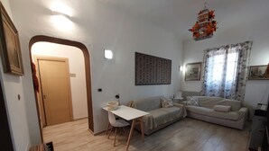 Een woonkamer met een bank, een bijzettafeltje en een stoel. Er is een deur die naar een andere kamer leidt.