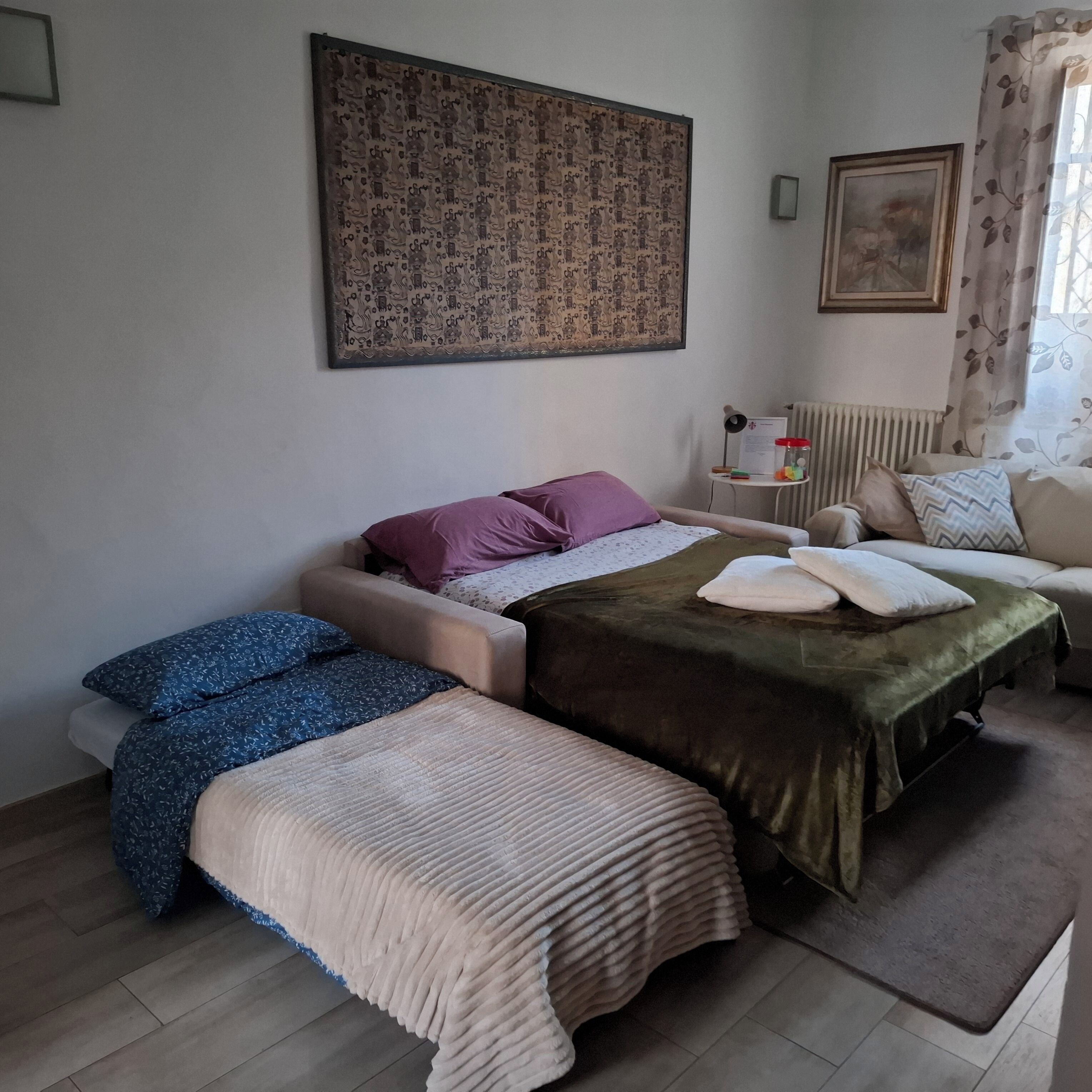 A bedroom with a bed, two bedside tables, a radiator, and a window with curtains.