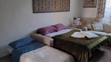 A bedroom with a bed, two bedside tables, a radiator, and a window with curtains.
