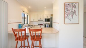 Una cocina moderna con armarios blancos, encimera de mármol y dos sillas de madera.