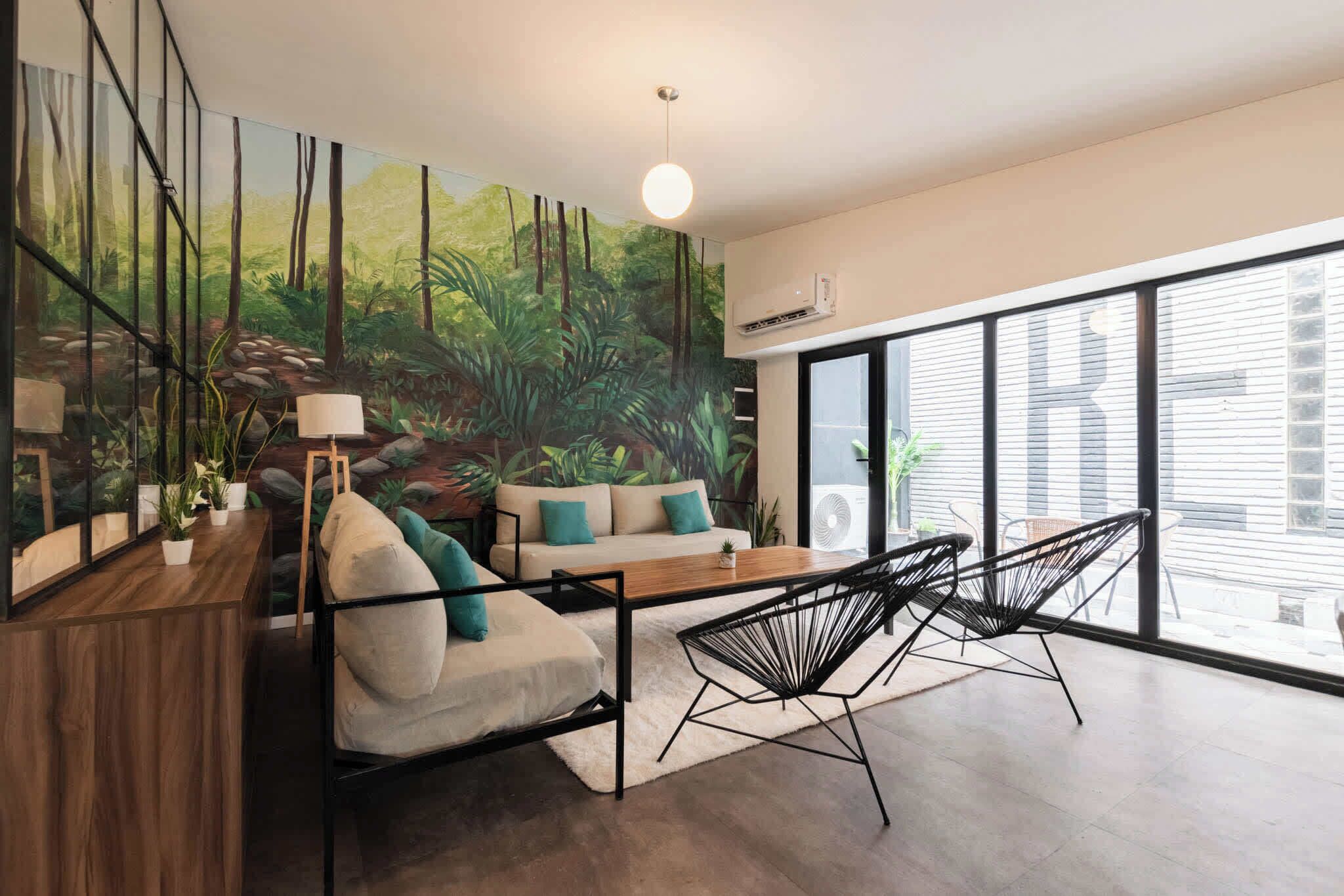 Una sala de estar moderna con un sofá, sillas, una mesa de madera y un cuadro grande de un bosque.