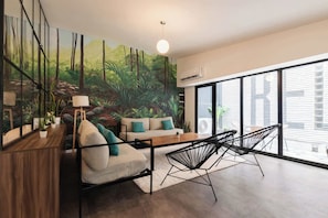 Una sala de estar moderna con un sofá, sillas, una mesa de madera y un cuadro grande de un bosque.