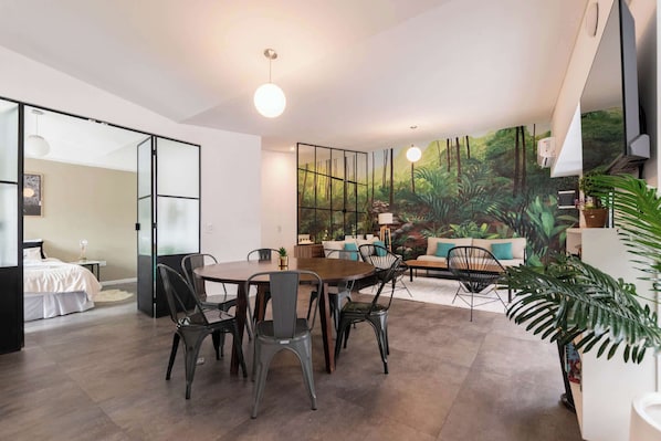 Una sala de estar moderna con comedor, un ventanal con un mural de bosque y un sofá con cojines.
