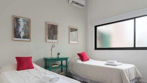 Een hotelkamer met twee bedden, een klein tafeltje met een lamp, en beelden in lijsten aan de muur.