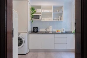 Uma cozinha compacta com arm ários brancos, micro-ondas, cafeteira e máquina de lavar.