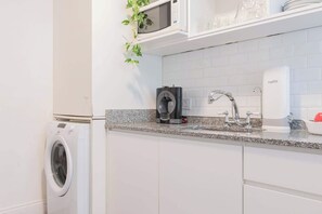 A compact kitchen with a washing machine, a coffee machine, and a sink.