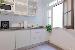 Una cocina moderna con armarios blancos, encimera de granito, cafetera y ventana con vistas.