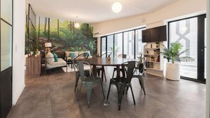 Een ruime eetruimte met een grote tafel en stoelen, omgeven door grote ramen en een muurschildering van een boslandschap.