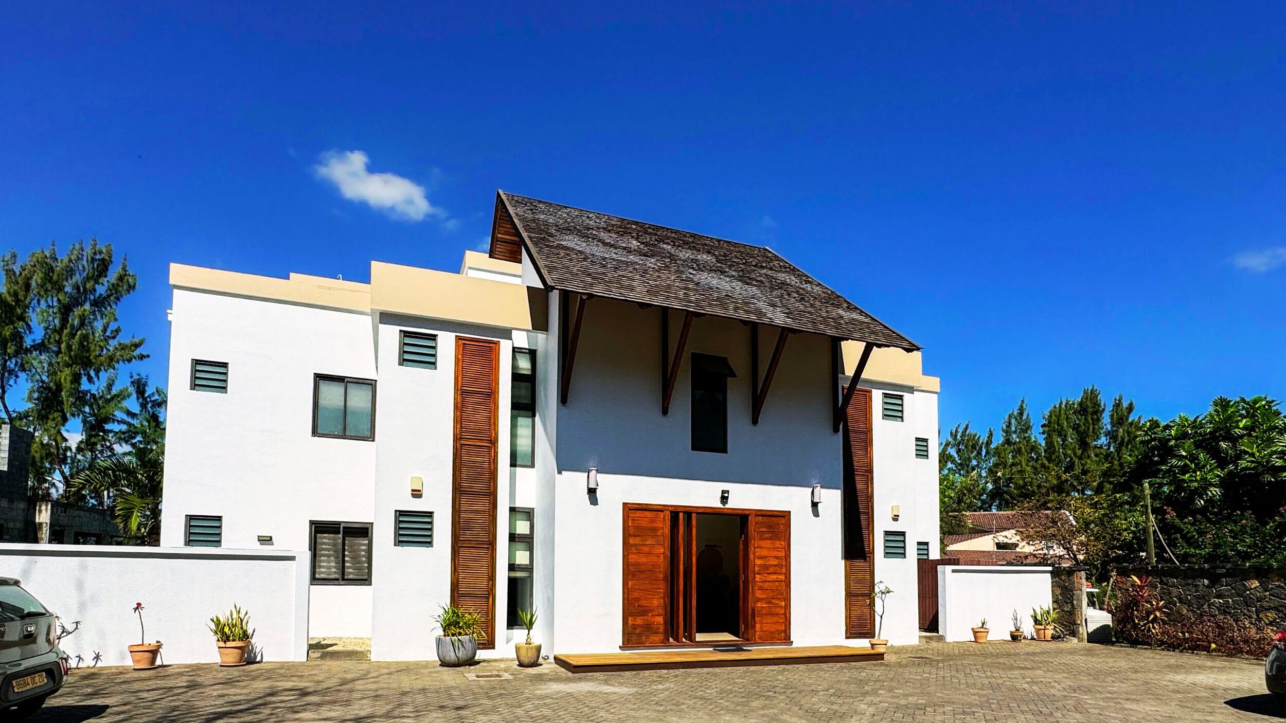 Ein modernes, zweistöckiges Haus mit flachem Dach, weißen Außenwänden und Holzjalousien.