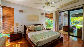 A bedroom with a bed, wooden floor, ceiling fan, and a view of a garden through a sliding glass door. - Olana Beach by Horizon Holidays (Black River)