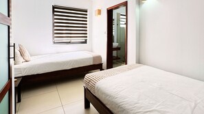 Ein Schlafzimmer mit zwei Einzelbetten, einem Fenster mit Jalousien, einem Spiegel und einem Nachttisch.