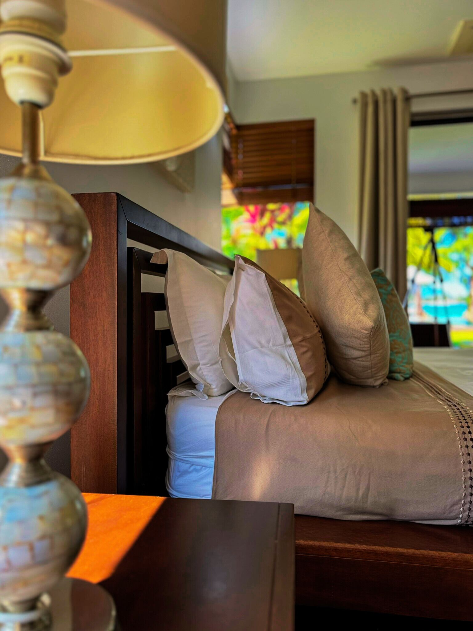 A neatly made bed with a wooden headboard, white and beige pillows, and a lamp with a globe base.