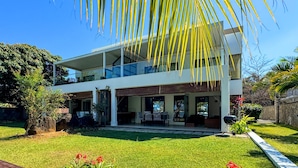 A modern two-story house with a balcony, a patio with outdoor furniture, and a well-maintained garden. - Olana Beach by Horizon Holidays (Black River)