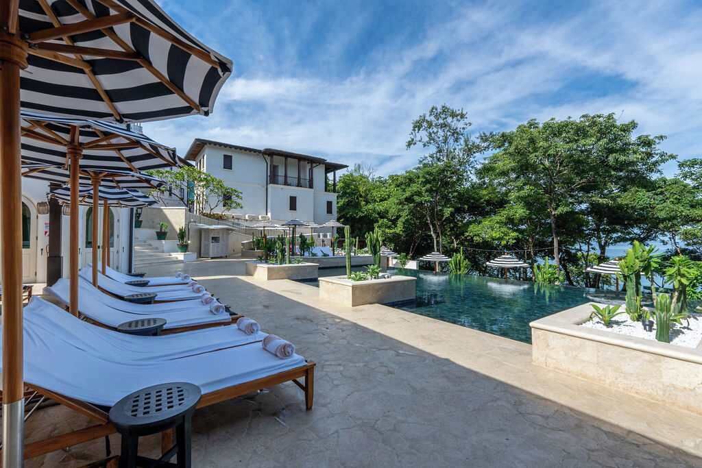A poolside area with lounge chairs and umbrellas, a clear view of the pool, and a building in the background.