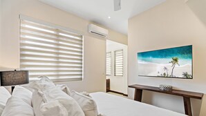 Une chambre d’hôtel avec un grand lit, un téléviseur à écran plat posé sur une console en bois, et un tableau sur le thème de la plage accroché au mur.