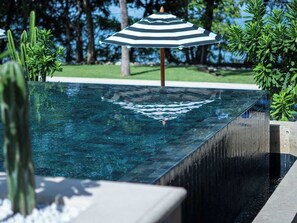 A clear pool with a wooden deck and a striped umbrella. - Stylish Condo in the Heart of Las Catalinas with Vibrant Design & Exclusive Beach Club Access (Las Catalinas)