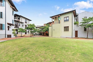 A courtyard with a grassy lawn, surrounded by multi-story buildings with balconies and windows. - Stylish Condo in the Heart of Las Catalinas with Vibrant Design & Exclusive Beach Club Access (Las Catalinas)