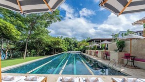 Un espace aménagé au bord de la piscine, avec des chaises longues et des parasols, entouré de verdure et surplombé par un ciel dégagé.