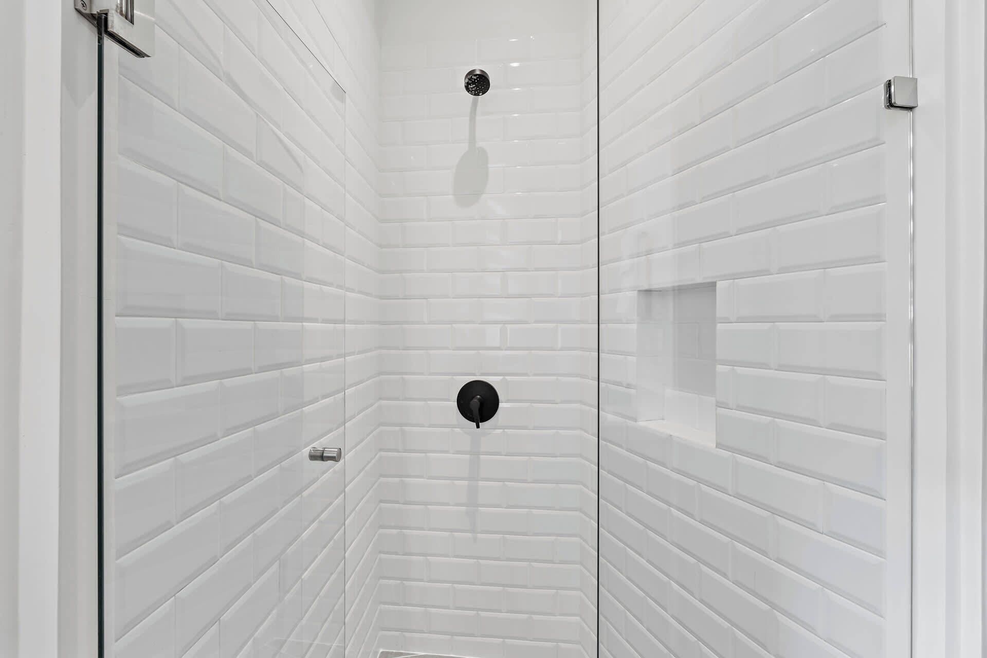A shower with white tiled walls and a black showerhead.
