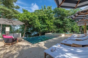 A poolside area with lounge chairs and umbrellas, surrounded by lush greenery.