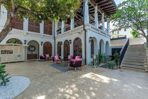 A courtyard with a covered seating area, a staircase, and a building with arched windows and a balcony. - Stylish Condo in the Heart of Las Catalinas with Vibrant Design & Exclusive Beach Club Access (Las Catalinas)