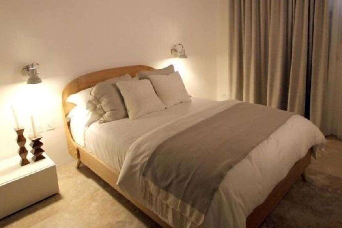 Een slaapkamer met een houten bed, twee bedlampen en een groot raam met gordijnen.