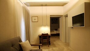 A cozy living room with a sofa, a dining table with chairs, and a TV mounted on the wall. - The King George Village Boutique Living (Hal Gharghur)