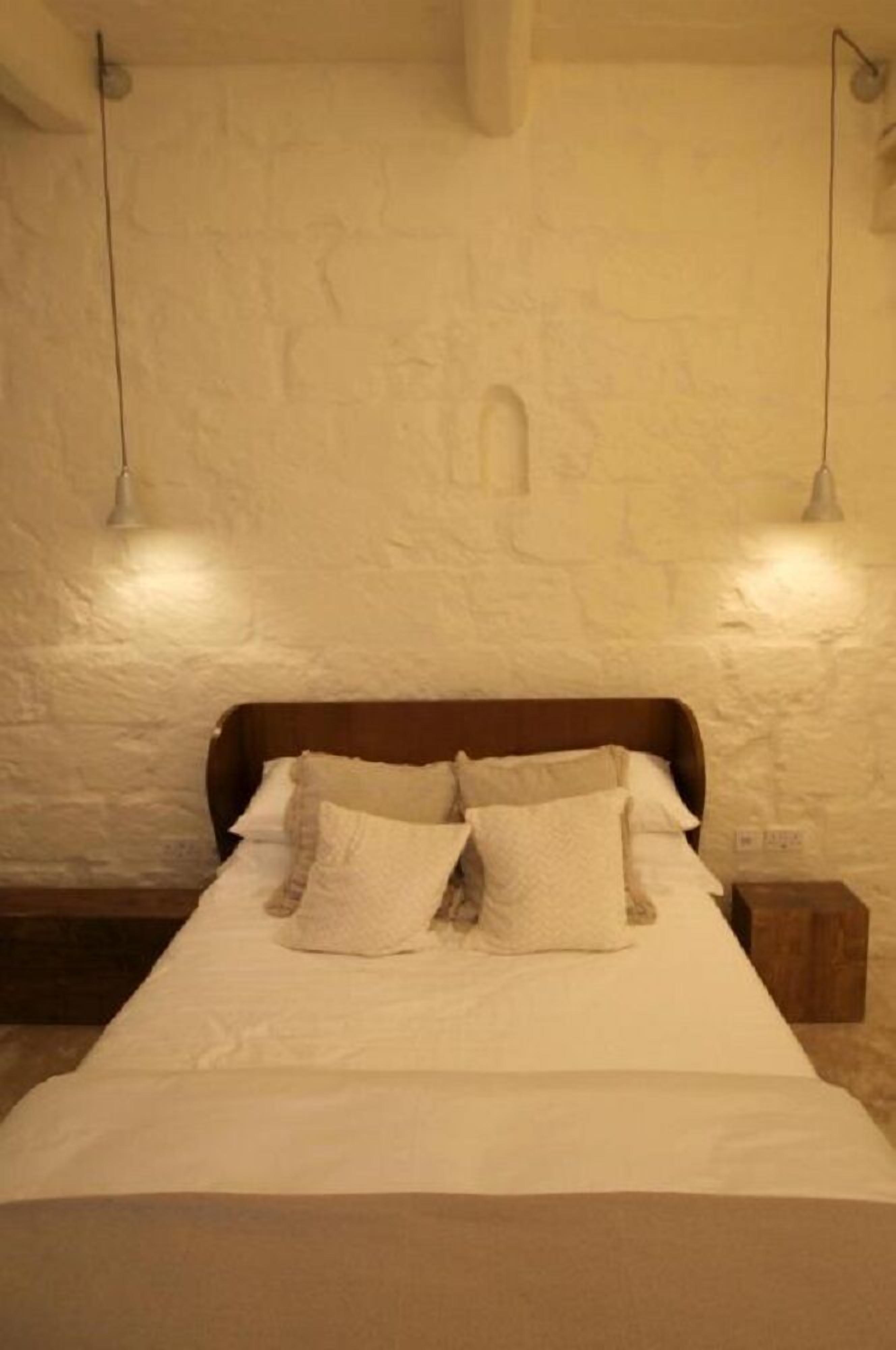 Een bed met witte lakens en kussens, een houten hoofdbord en twee hanglampen.