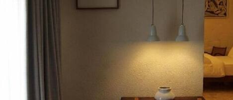 Un coin repas avec une table, des chaises et des luminaires suspendus. Un tableau encadré orne le mur et un vase est posé sur la table.