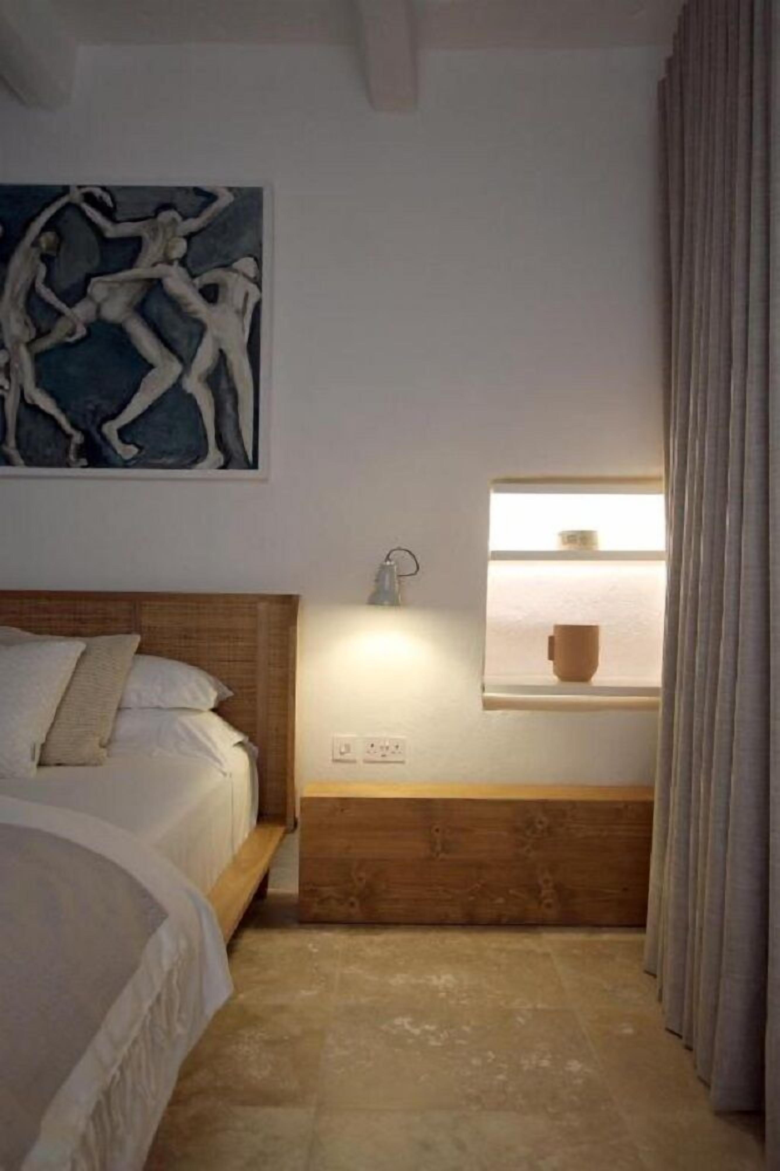 A bedroom with a bed, a wall-mounted light, a window with a view, and a painting.