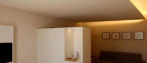 Un dormitorio con cama, armario, mesita de noche y televisor en la pared.