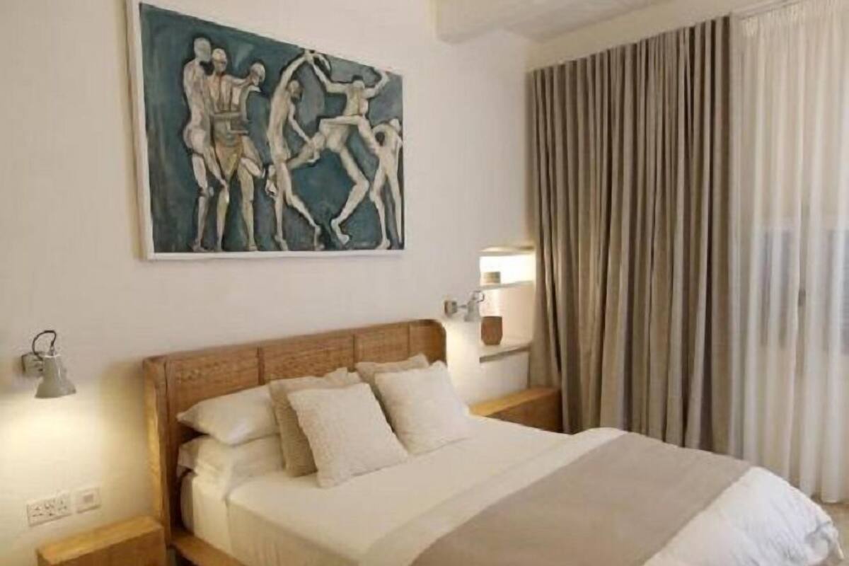 Een slaapkamer met een houten bed, een nachtkastje, een wandlamp en een schilderij.