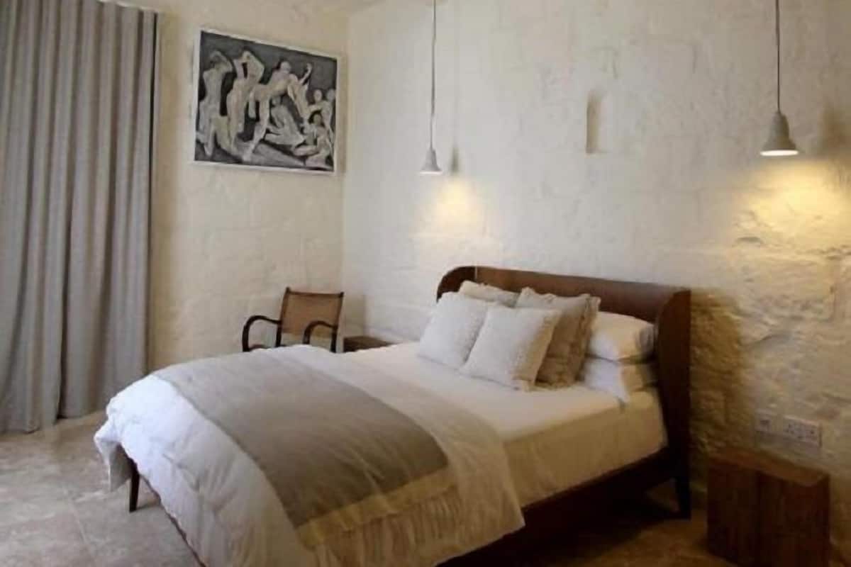Een slaapkamer met een bed, een stoel, een schilderij en een nachtkastje.