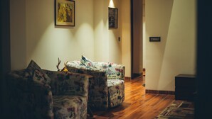 Un pasillo con un sofá y sillones, piso de madera y dos luces fijadas a la pared.
