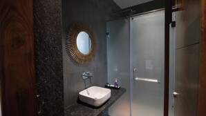 Un baño moderno con encimera de granito, un lavamanos blanco, un espejo redondo y un box de ducha de vidrio.