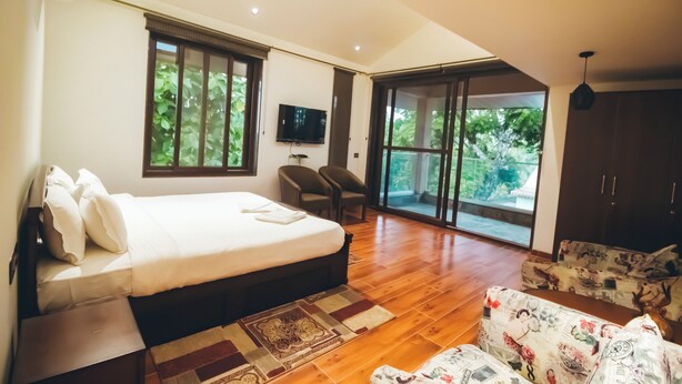Un dormitorio con cama, televisor, escritorio y silla. Cuenta con un ventanal grande y una puerta que da a un balcón.