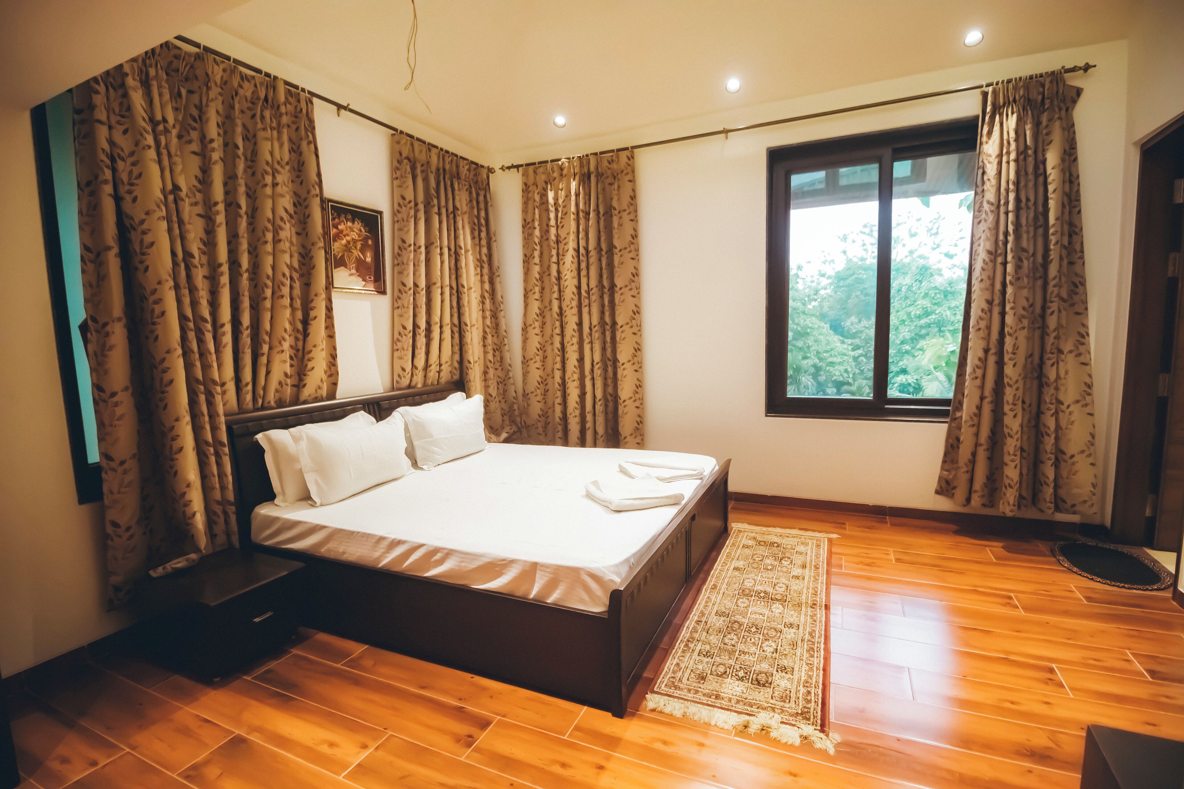 A bedroom with a wooden floor, a bed with white linens, and a window with curtains.