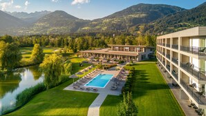 A hotel with a swimming pool, outdoor seating, and a view of the surrounding mountains and lake. - Dolomitengolf Suites (Lavant)