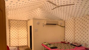 Una habitación pequeña y funcional con una cama individual, una silla roja y un ventilador de techo.