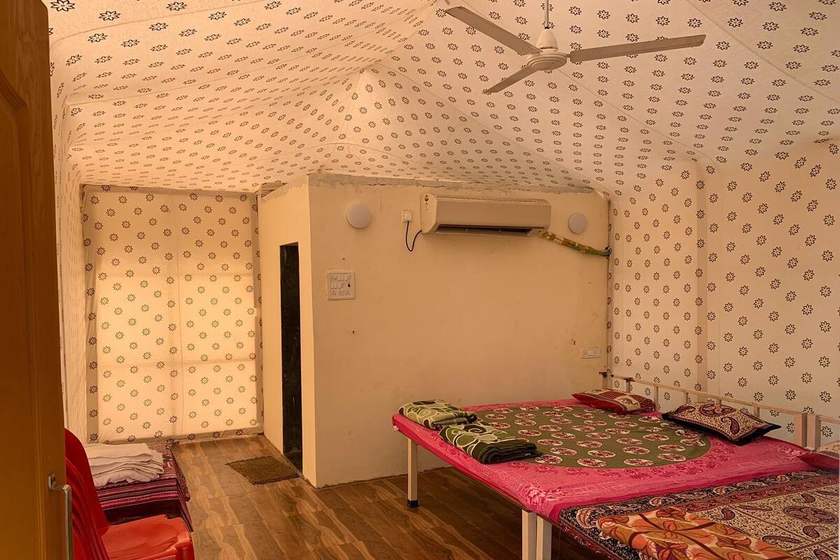 A small, compact room with a single bed, a red chair, and a ceiling fan.