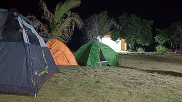 Un campamento nocturno con tiendas de campaña y un edificio al fondo.