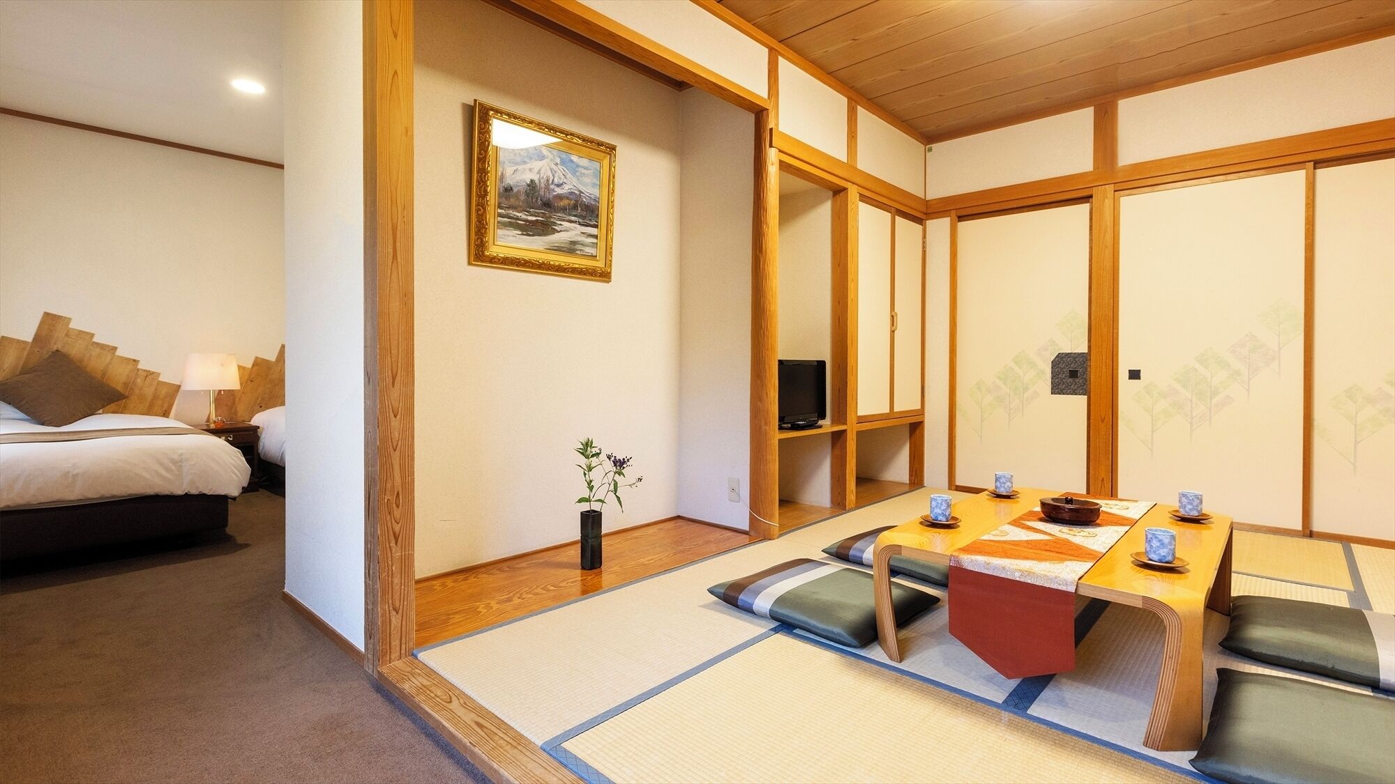 Una habitación tradicional japonesa con suelo de tatami, un futón, una televisión y una mesa de comedor con cojines.