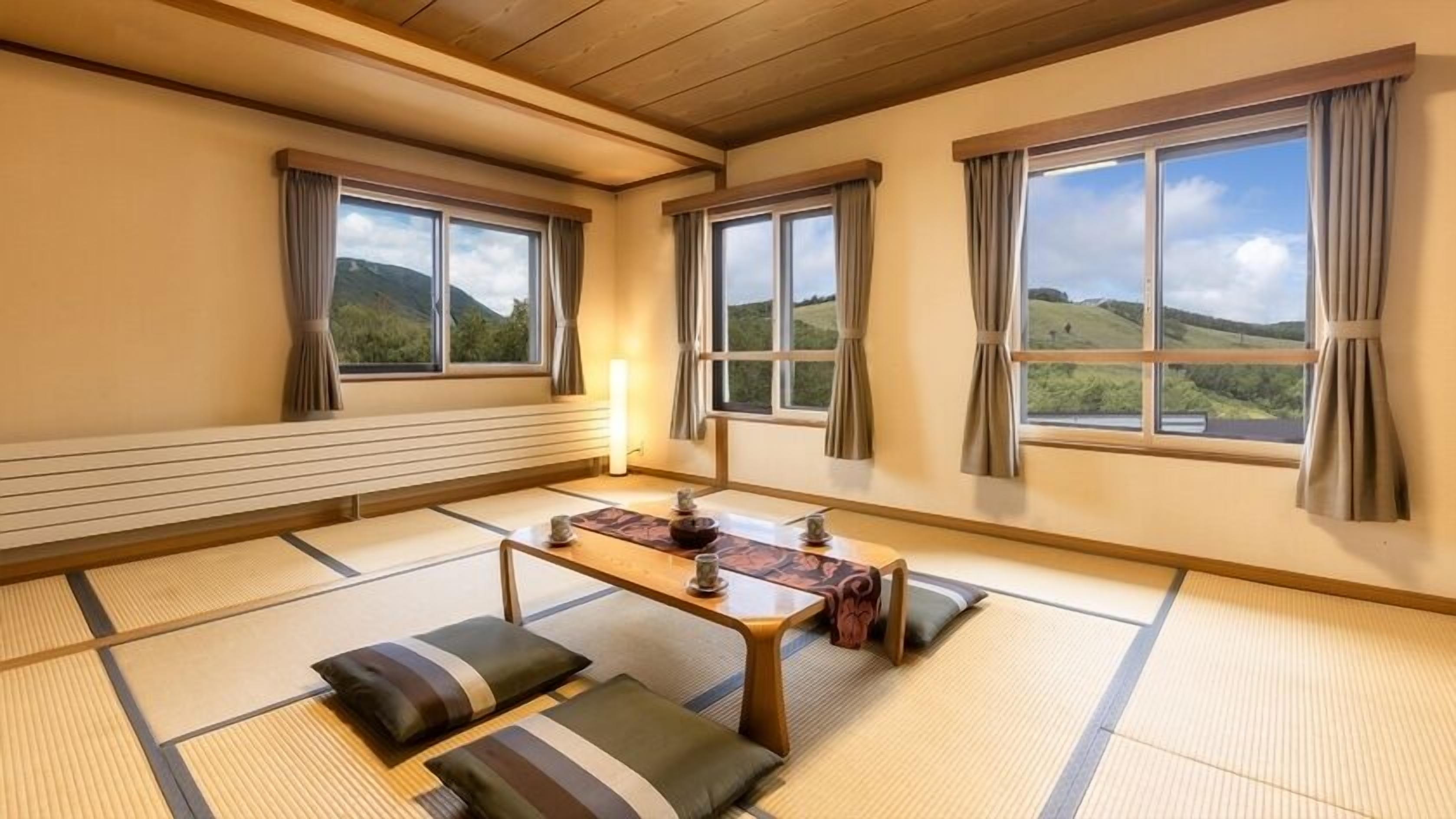 Una habitación con suelo de tatami, una mesa baja, cojines y ventanas amplias con cortinas.