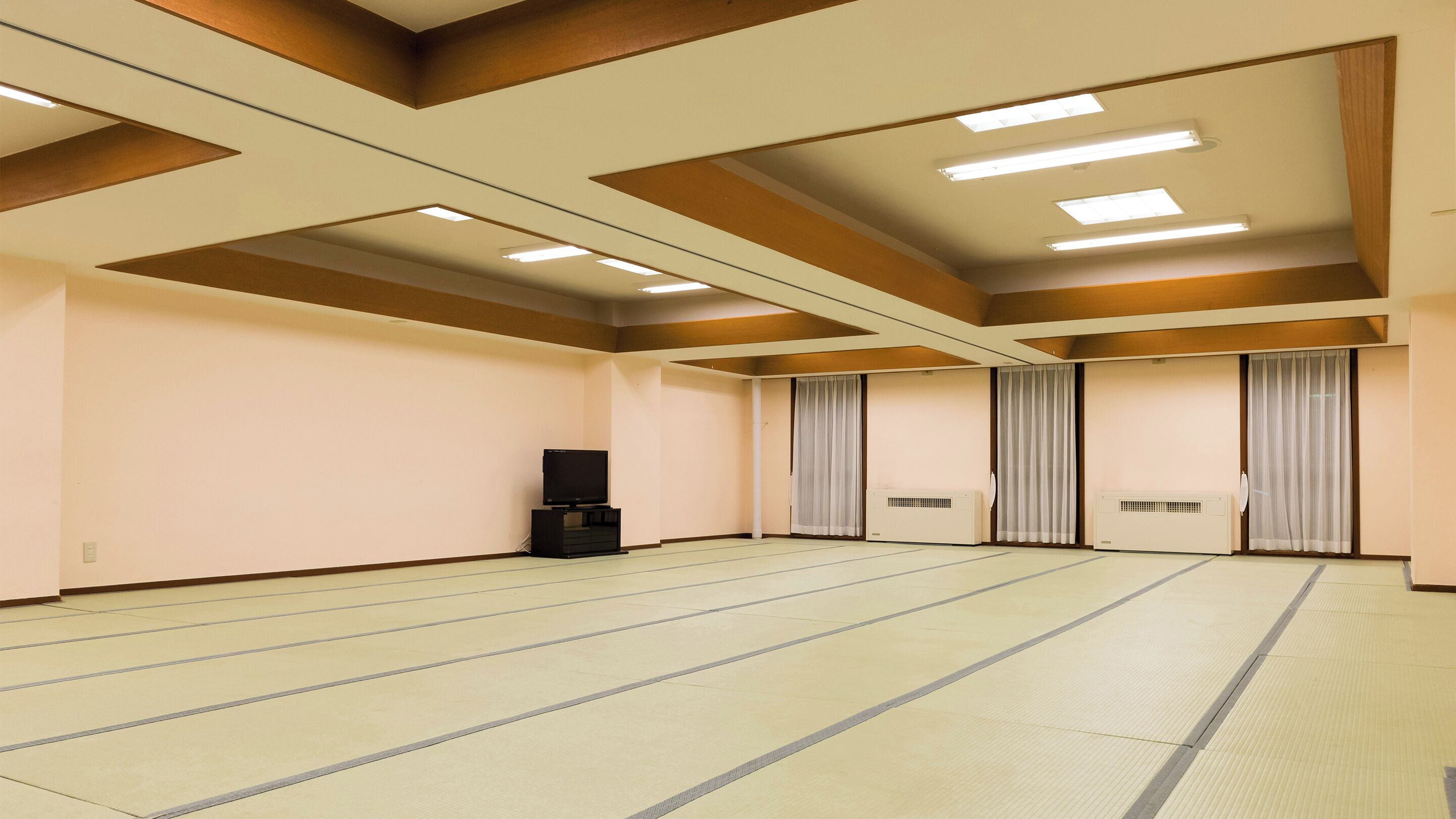 Una habitación amplia y vacía con esteras de tatami, un televisor y puertas correderas.