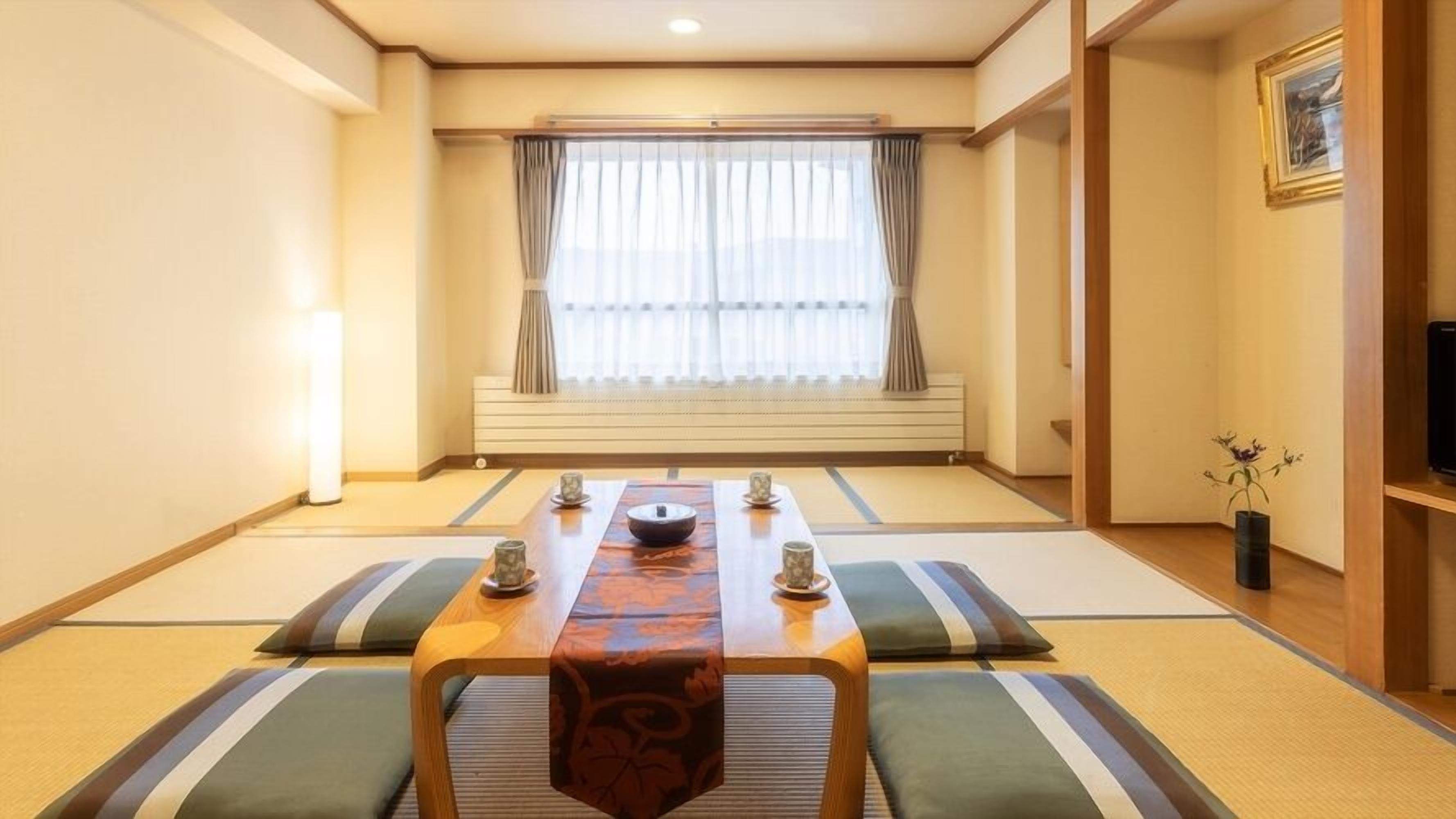 Una habitación tradicional japonesa con suelo de tatami, una mesa baja con camino decorativo, cojines y una puerta corredera que da a otra habitación.