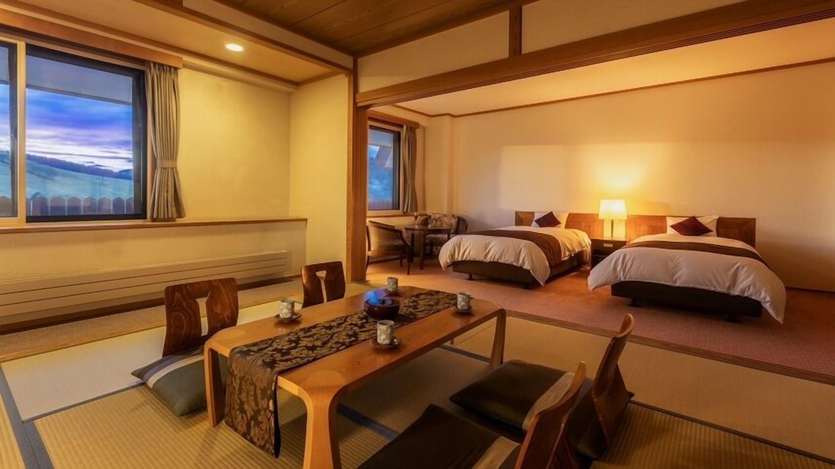 Et traditionelt japansk hotelværelse med tatamigulv, et lavt bord med en vævet måtte, to senge med træsengegavle og udsigt over landskabet gennem store vinduer.