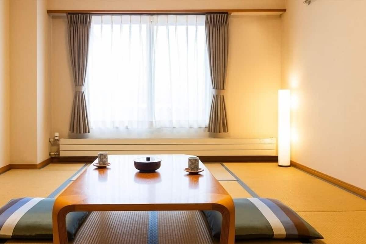 Una stanza con pavimento in tatami, un tavolino con una ciotola, due tazze e una lampada da terra.